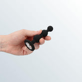 A hand holds the Shots America Diamond Butt Plug – Wearable Silicone Beads in black, featuring three graduated silicone beads and a flared base, set against a light gradient background.